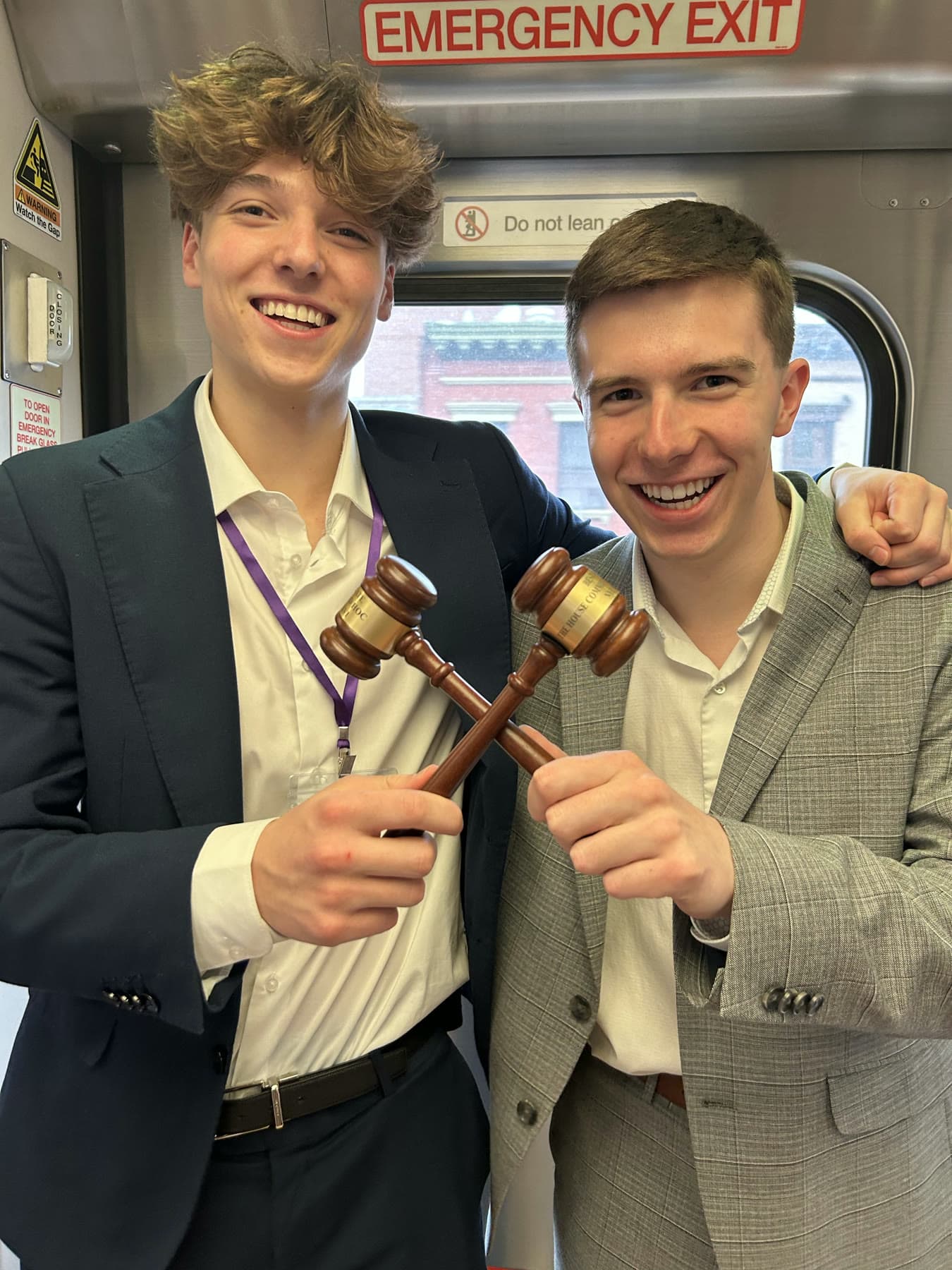 Two team members in suits on a train, grinning, each holding up a wooden gavel.