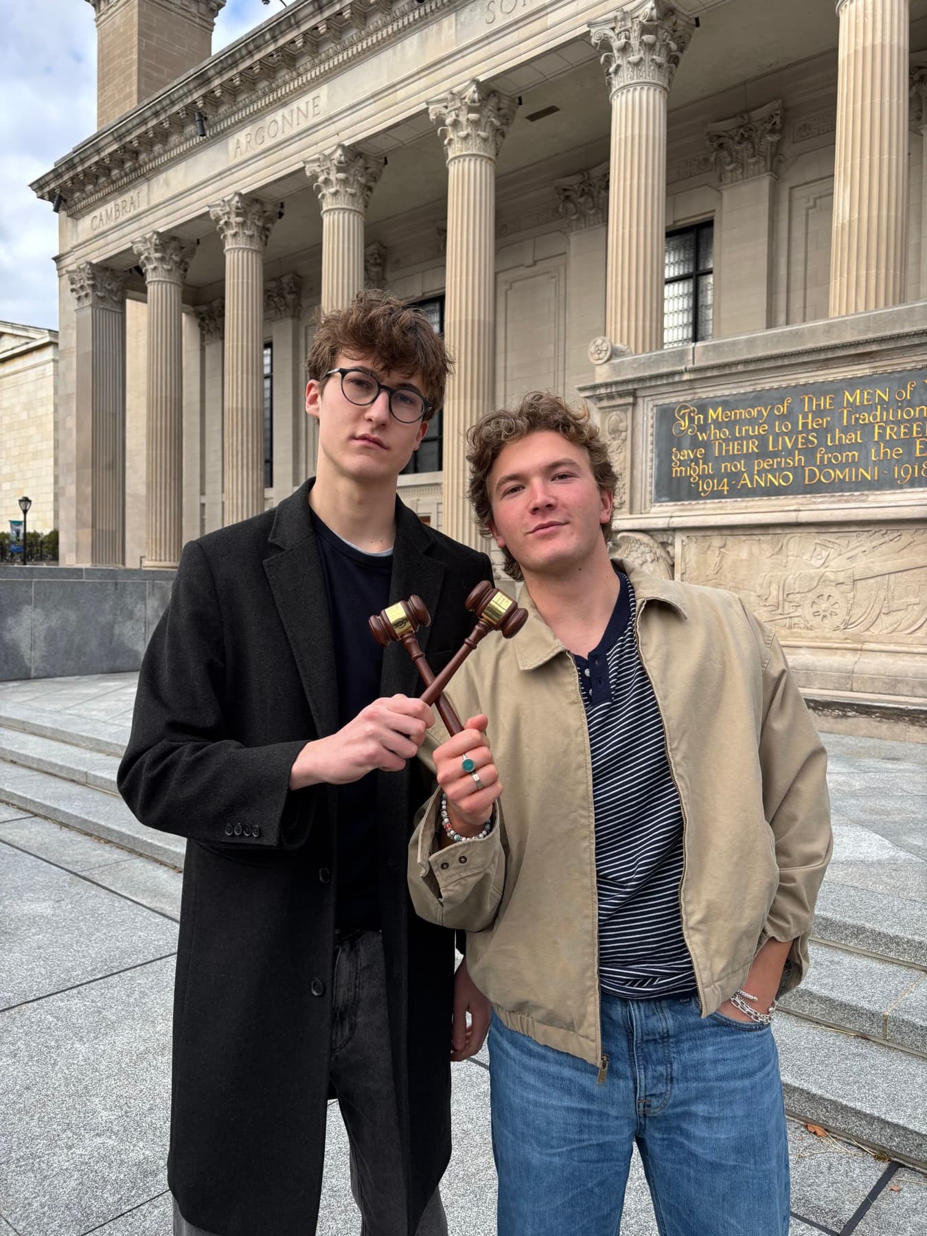 Two MUNTY members standing outside a columned building and holding crossed wooden gavels.