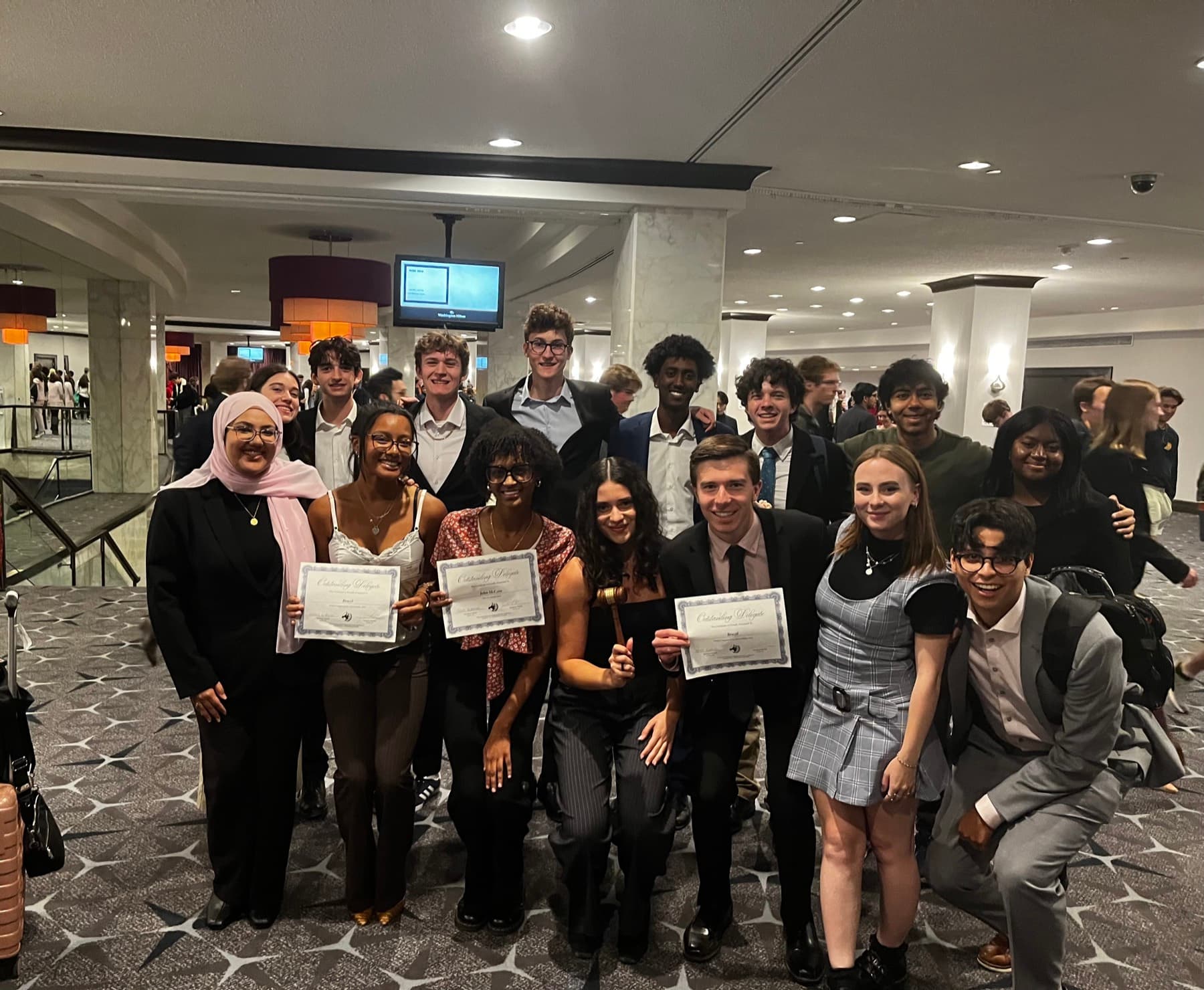 The Yale team gathered in a hotel lobby after an awards ceremony, three members holding Outstanding Delegate certificates.