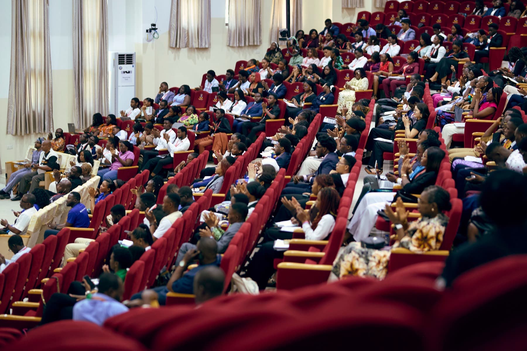 A large auditorium packed with delegates in the red seats, seen from one side.