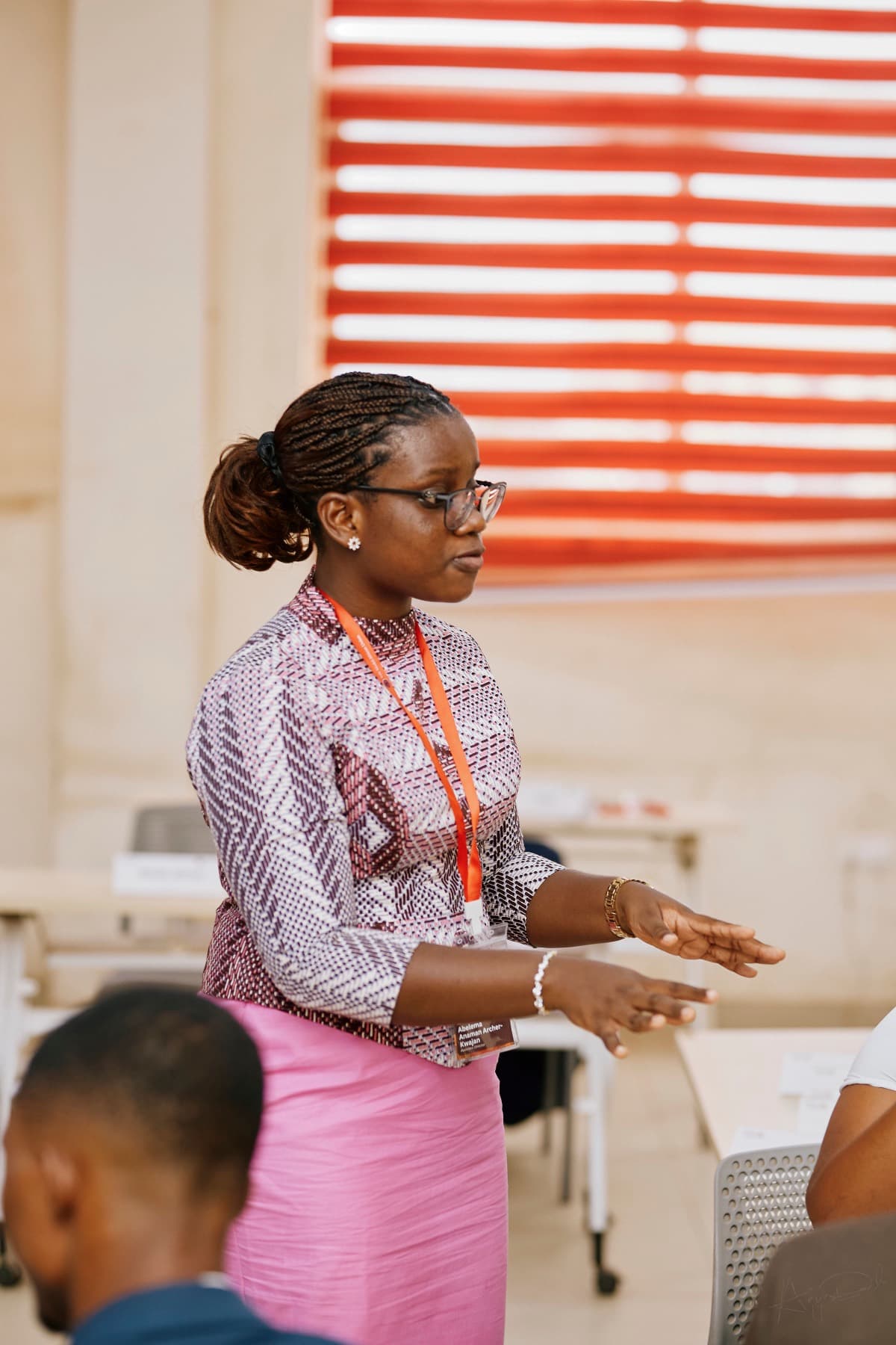 A delegate standing at her seat mid-sentence, one hand open in front of her, addressing a committee room.