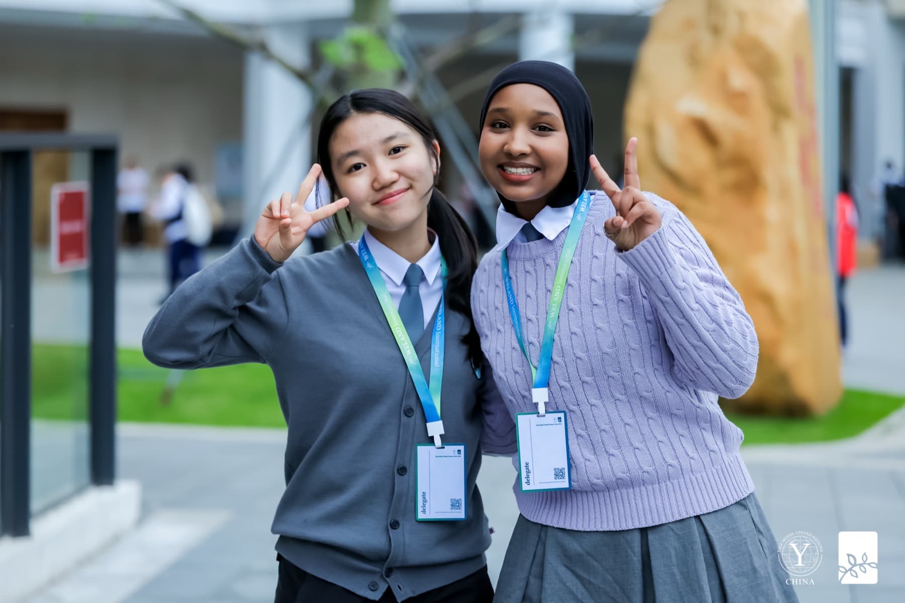 Two delegates standing outdoors between sessions, smiling at the camera, conference lanyards around their necks.