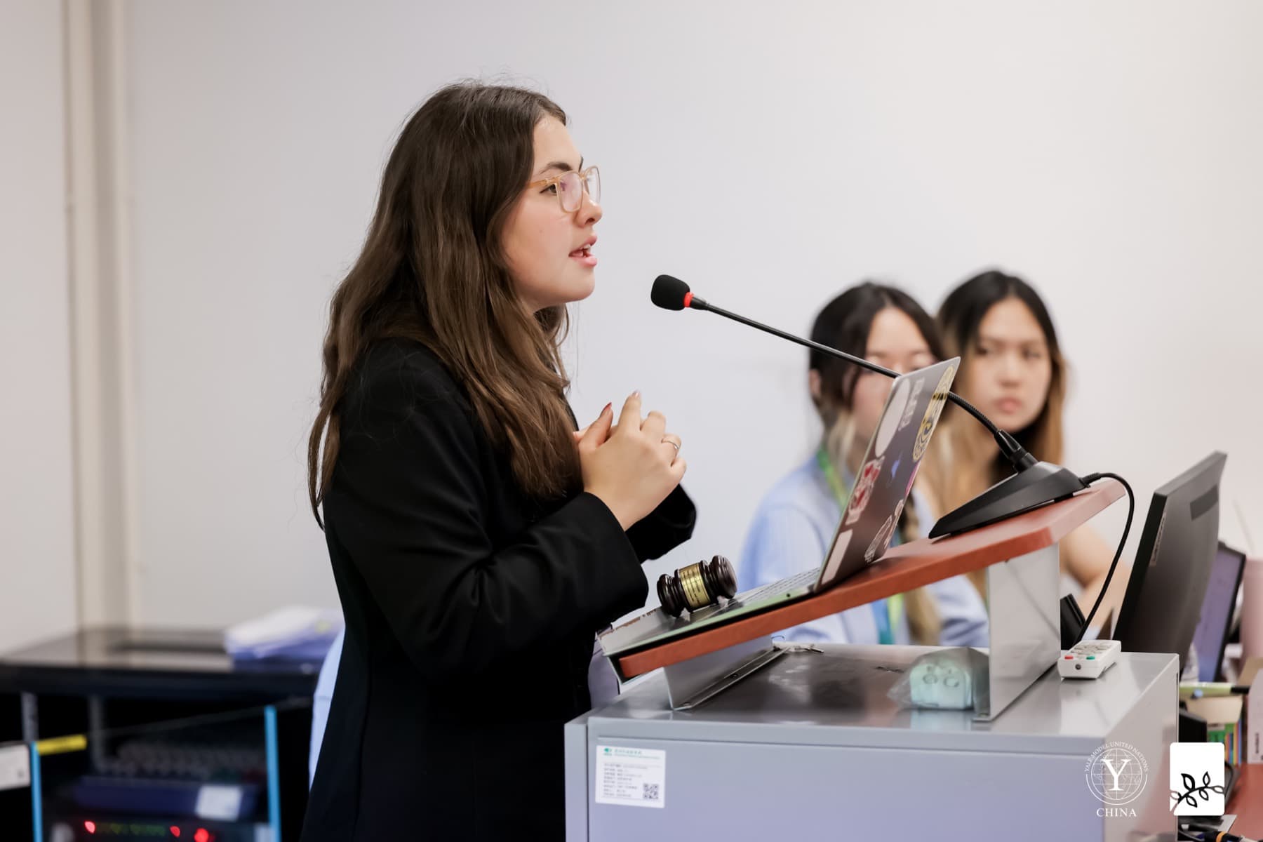 A delegate speaking into a microphone at a wooden podium, her notes in front of her.